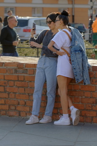 Two girls captured outdoors, in a public space, while interacting with a smartphone